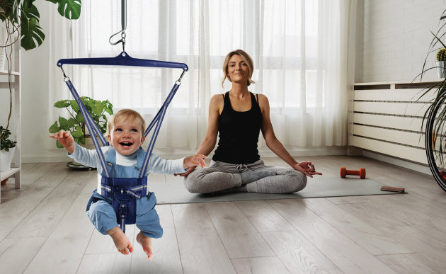 Smiling baby in Jolly Jumper holding mum’s hand during home workout or yoga