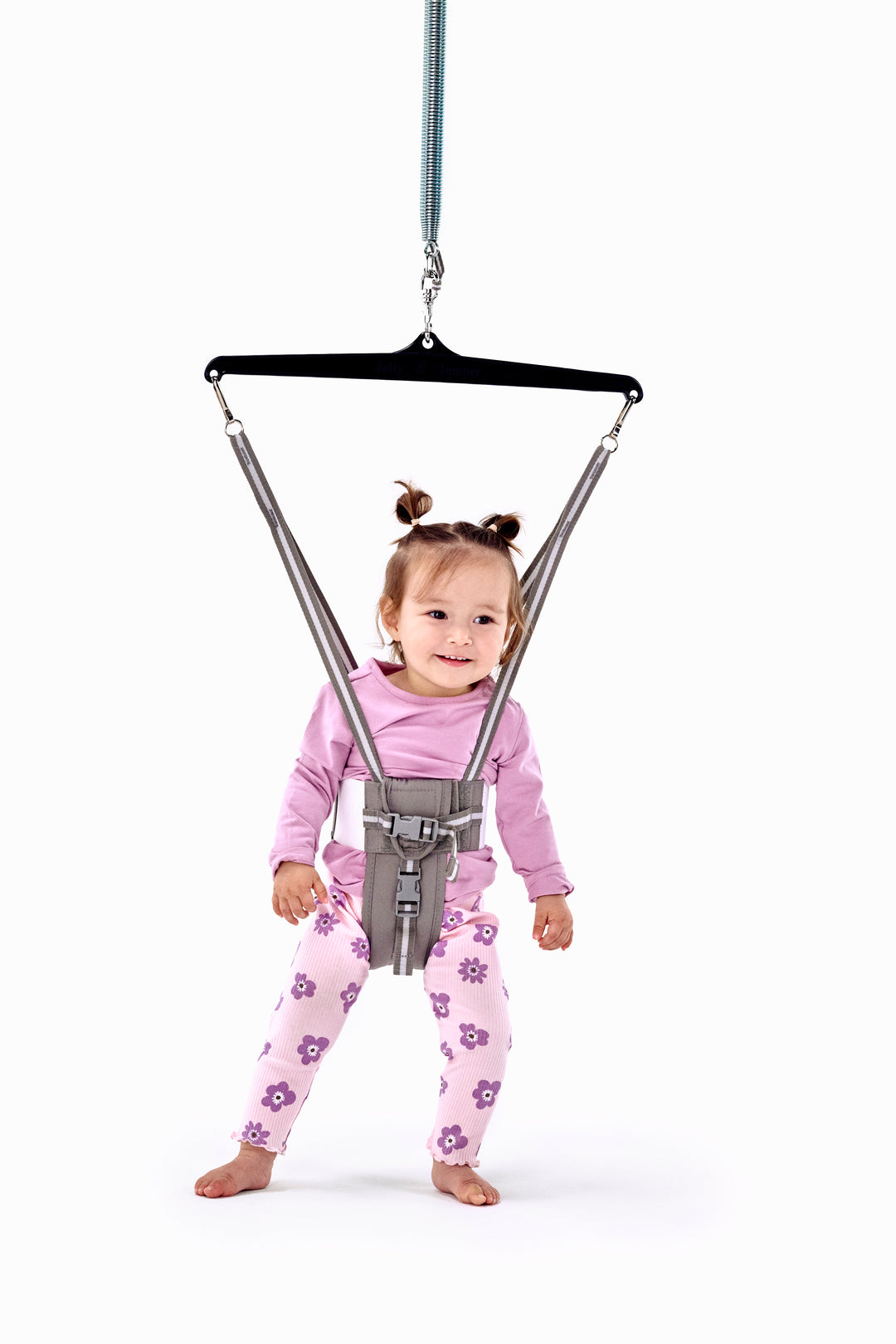 Toddler in pink top and floral leggings bouncing in the grey Jolly Jumper doorway bouncer